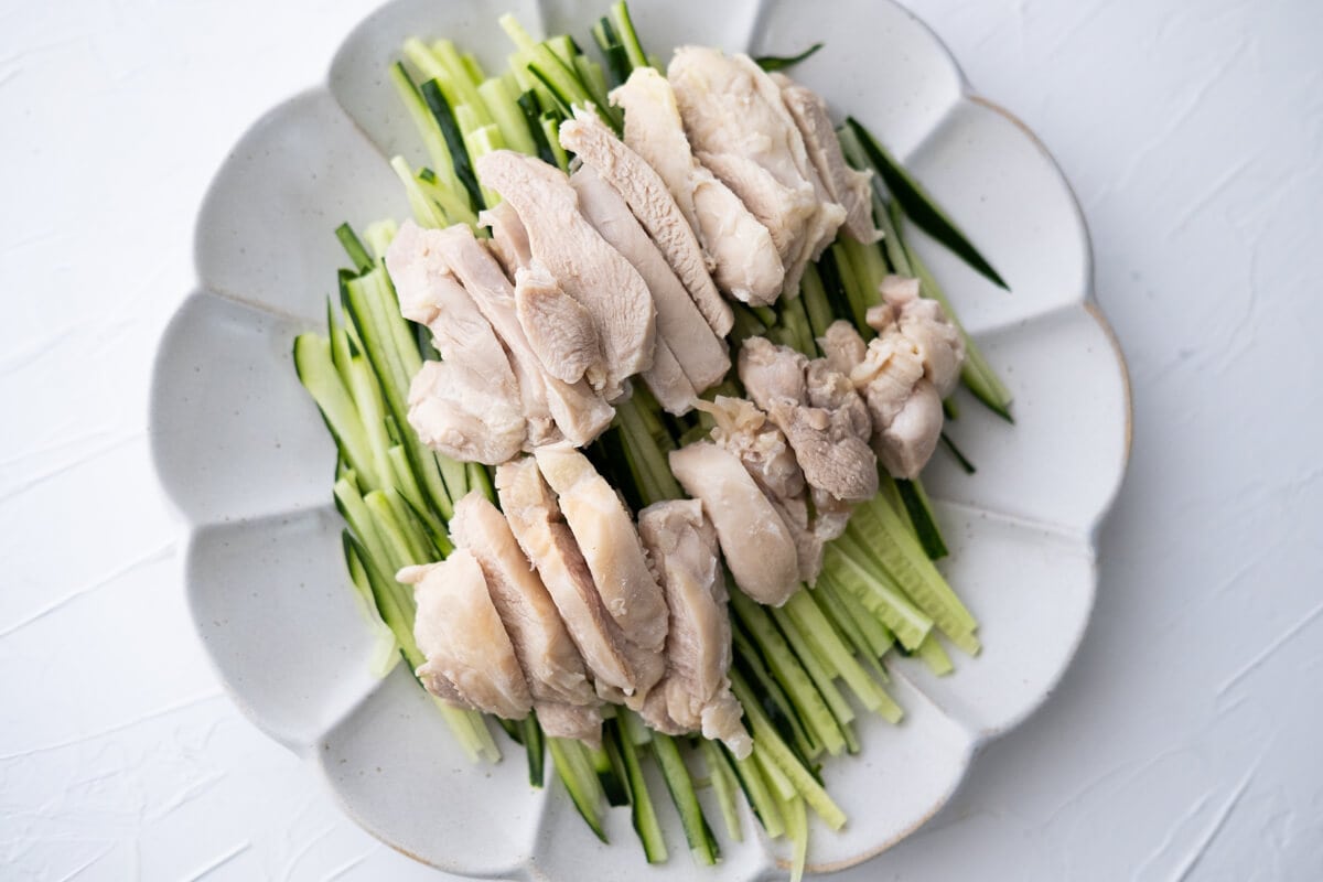 Skinless and boneless chicken tighs with shredded Japanese cucumber underneath it on a plate. 