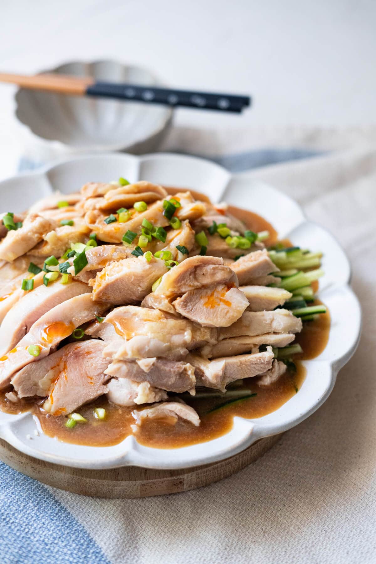 Tender chicken with sesame sauce drizzle on top, shredded Japanese cucumber underneath, and chopped green onions sprinkled on top served in a white plate. 
