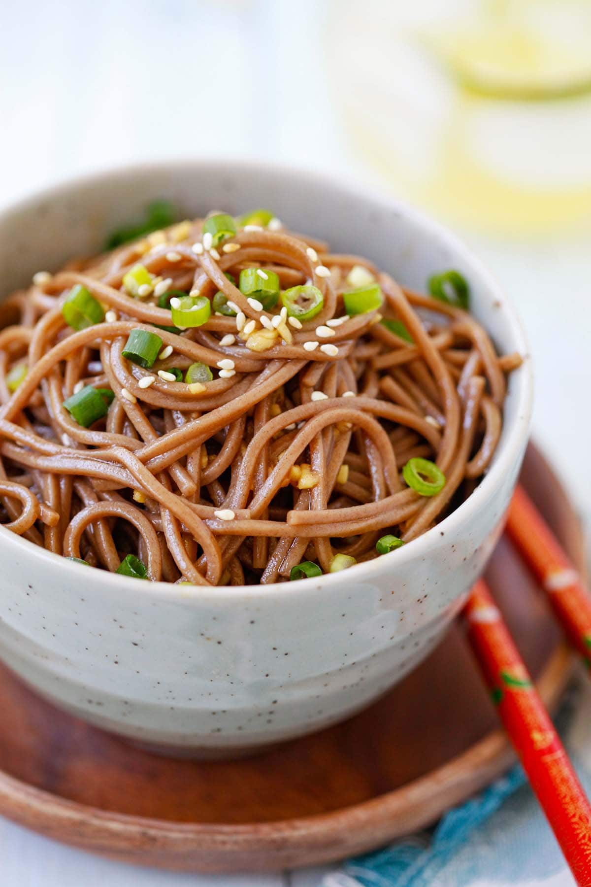 Soba noodles with ginger and soy served in a bowl with white sesame and green onions sprinkled on top. 