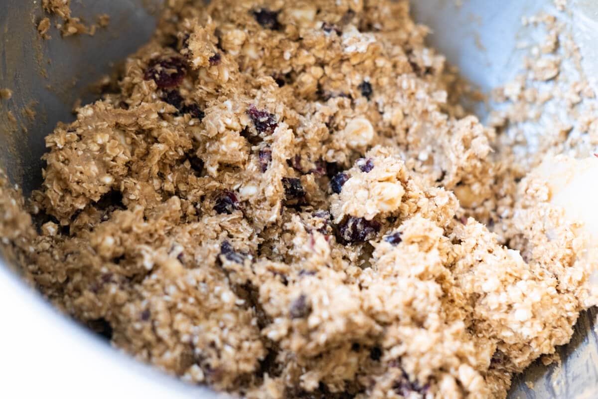 Oats, dried cranberries, and chocolate chips combined with dough in a mixing bowl. 