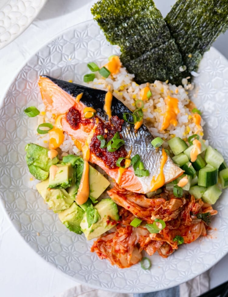 Salmon rice bowl with baked salmon, cubed avocado, cucumber, spicy kimchi, and topped with Sriracha mayo sauce and nori.