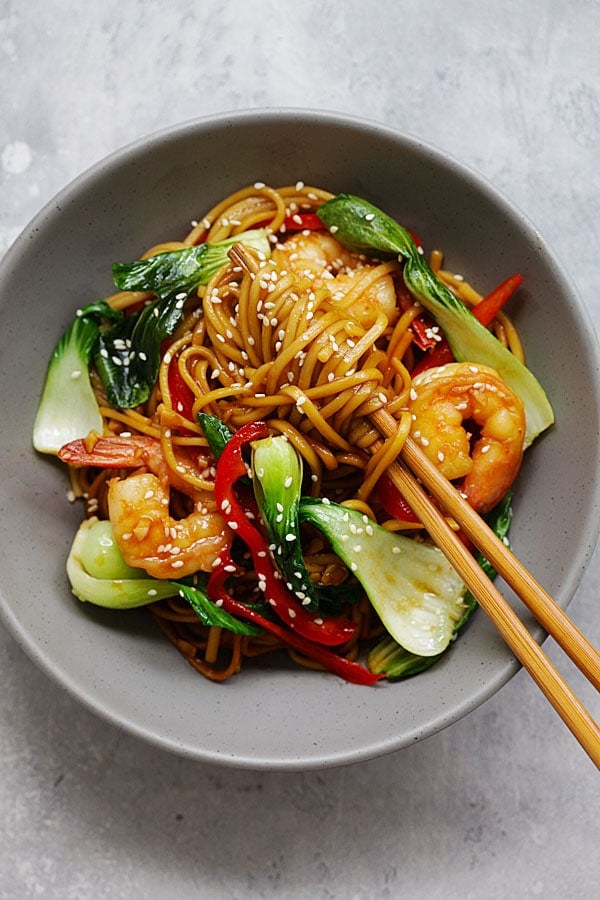 Lo mein noodles with shrimp being picked up by a chopstick.